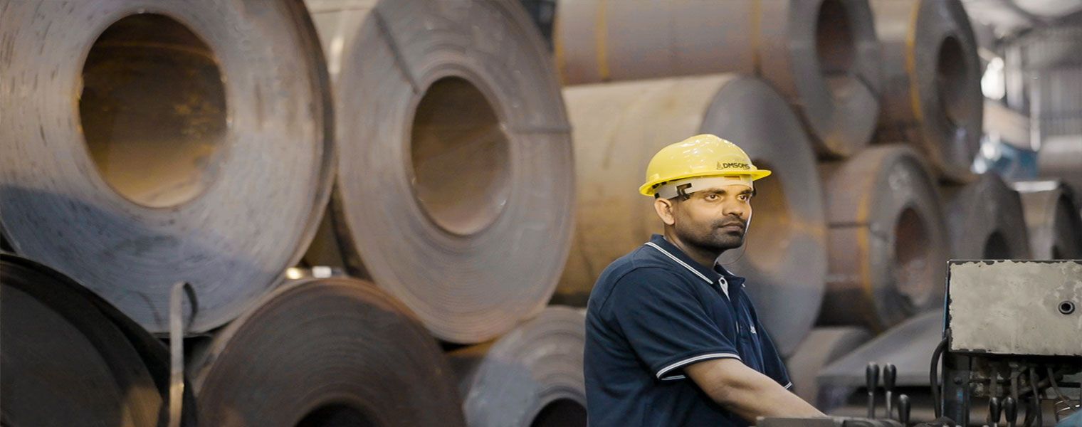 Dmsons worker in a hard hat beside stacked steel coils